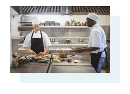 Two cooks prepare vegetables in a professional kitchen